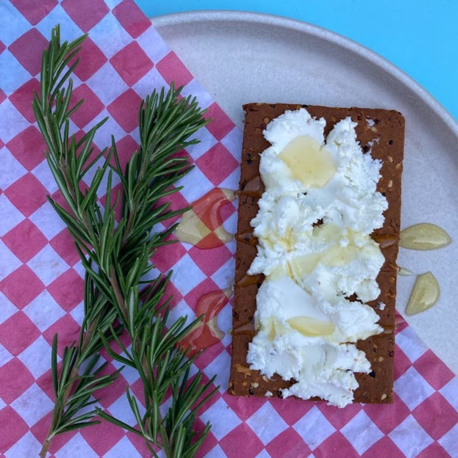 Fello Spicy PIzza Protein Bar Topped with Goat Cheese and Honey next to herbs.