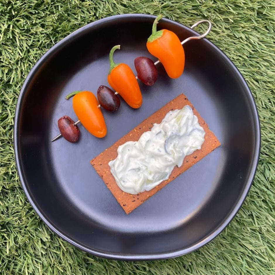 Fello Zesty BBQ Protein Bar topped with tzatziki and served with skewer of olives and peppers.