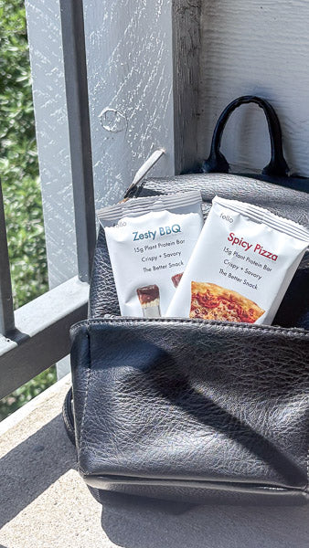 Two protein bars packed into the front pocket of a black backpack on a balcony.