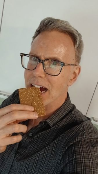 Man wearing glasses taking a bite of a tasty protein bar for a quick workday snack.