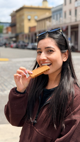 Woman smiling and eating a nutritious on-the-go protein bar while walking down a city street.