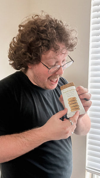 Man with curly hair inspecting a savory protein bar wrapper indoors.