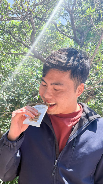 Man taking a bite of a healthy protein bar outdoors on a sunny day.
