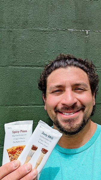 Smiling man holding Zesty BBQ and Spicy Pizza flavor savory protein bars.