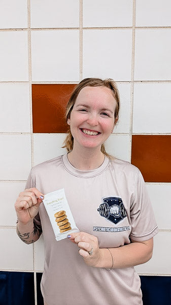 Smiling woman in gym athletic wear holding up an Everything Bagel flavor protein bar.